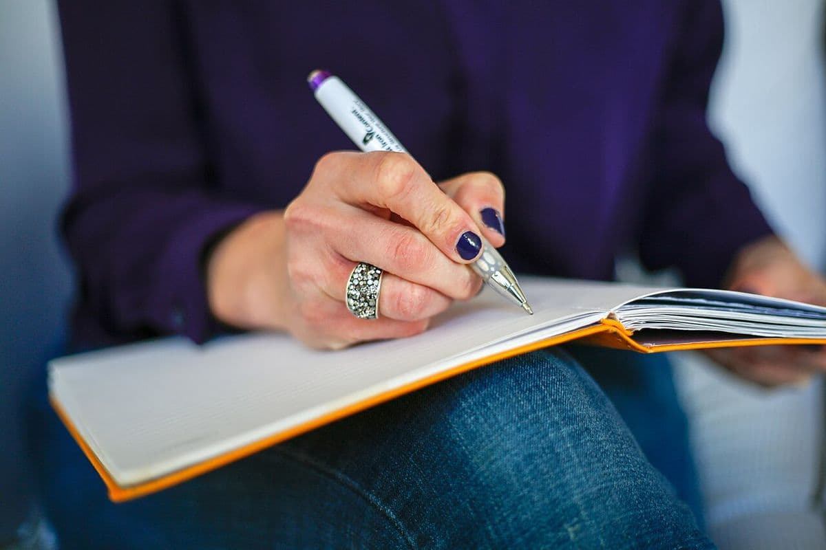 A person writing notes in an open notebook on their lap